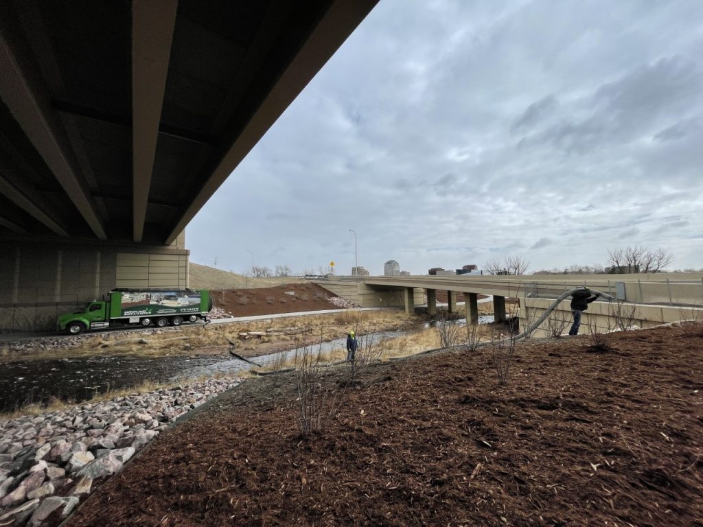 Ground Solutions blower truck applying mulch for erosion control under a bridge overpass.