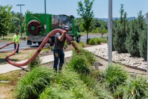 Ground Solutions technician using a pneumatic blower hose to precisely install mulch in a decorative landscape bed with ornamental grasses.