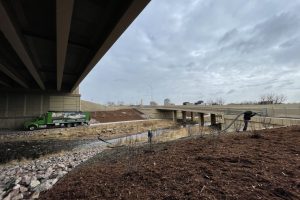 Ground Solutions blower truck applying mulch for erosion control under a bridge overpass.